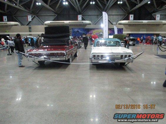Two classic cars, a red convertible and a white coupe, parked indoors