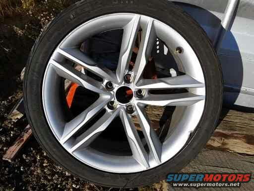 Silver alloy wheel with five split spokes and a black tire, resting on wooden planks