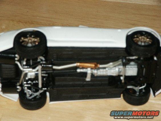 Underside view of a white car model, showing the exhaust and suspension components
