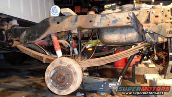 Rear leaf spring suspension with red shocks and brake drum on a vehicle undergoing repair