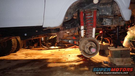 White vehicle's front suspension with red shocks and coil springs, lifted on blocks