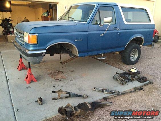 Blue Ford Bronco on jack stands with front suspension parts removed and laid out on the ground