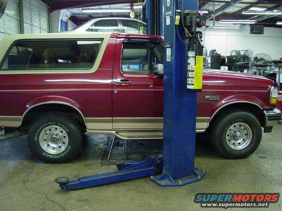 Red Ford Bronco on a lift in a garage. Bronco badge visible on the fender