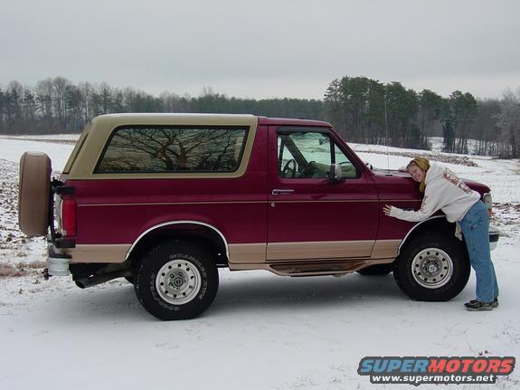 Maroon and tan Ford Bronco with a spare tire on the back, parked in the snow