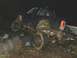 1978 Ford Bronco - Off-road vehicle tires are caked in mud as it climbs over large rocks in the dark.