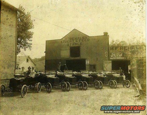 Several early cars parked in front of a building labeled 'J.H. REMALEY LIVERY & FEED STABLE' and 'M.F. REMALEY Ford SALES & SERVICE'
