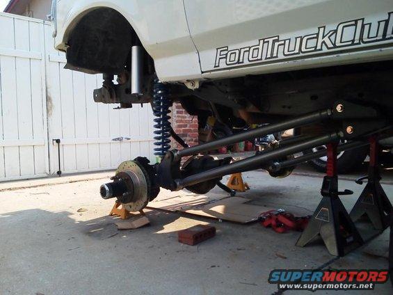 White Ford truck with front suspension removed, sitting on jack stands. "FordTruckClub" decal visible on the side
