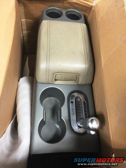 Tan leather-covered center console with dual cup holders and a chrome gear shifter, inside a cardboard box