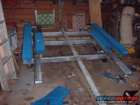 Boat trailer frame with blue carpeted bunks inside a garage