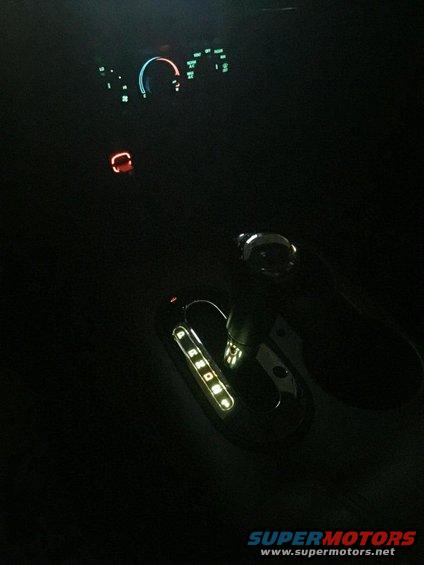 Interior shot of an automatic transmission shifter with illuminated gear selection and dashboard lights glowing in the dark