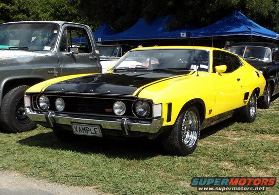 Front view of a yellow and black muscle car parked next to a truck