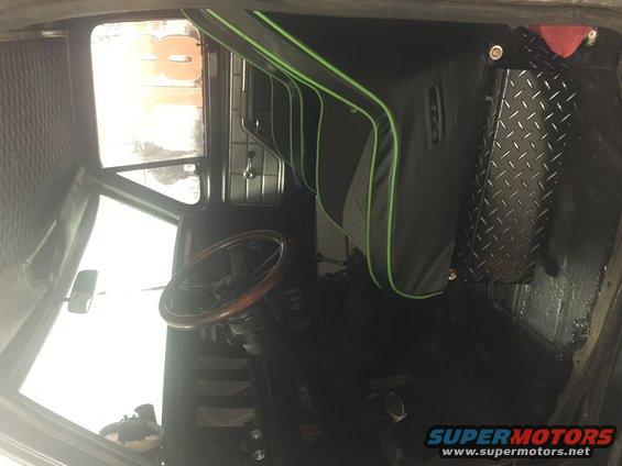 Vehicle interior with wood steering wheel, black seats with green trim, and diamond plate paneling