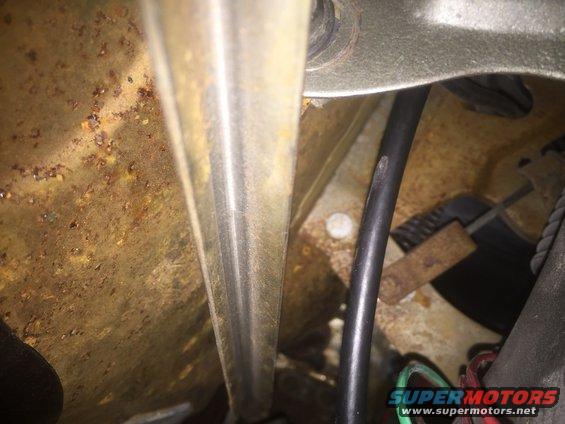 Close-up of rusty metal, a black cable, and some wiring in what looks like an engine bay