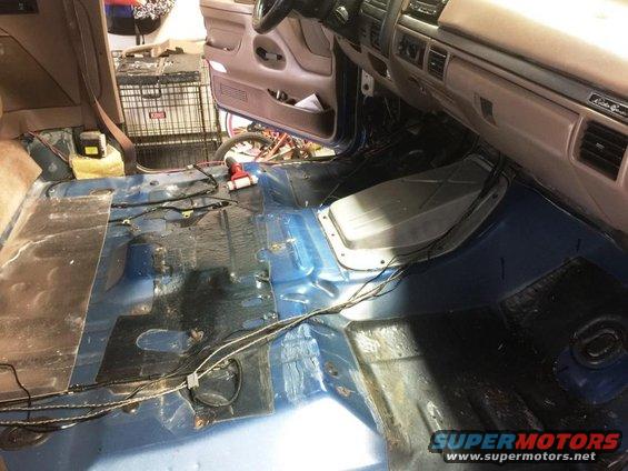 Interior of a vehicle with carpet removed, showing blue floor and exposed wiring