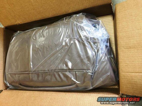 Brown car seat cover in plastic wrap inside a cardboard box