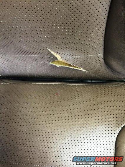 Perforated brown leather car seat with a large tear revealing yellowing material underneath