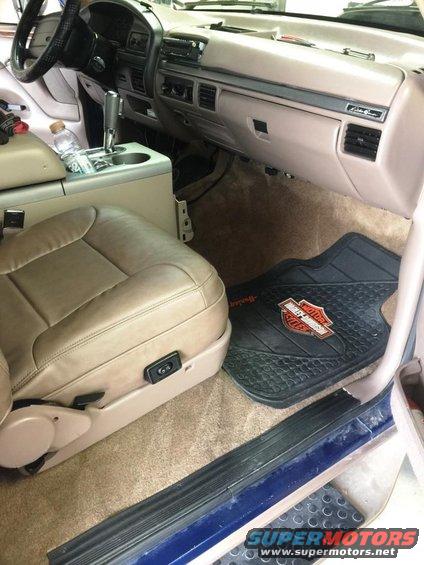 Interior shot of a truck's passenger side, showing tan leather seat, dashboard, and a Harley-Davidson floor mat