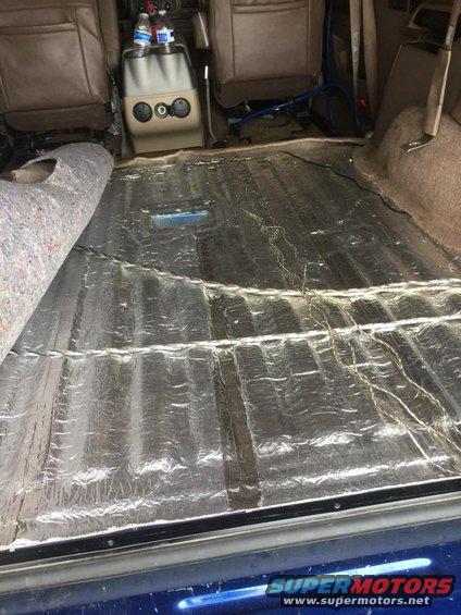 Vehicle interior showing soundproofing material installed on the floor, with seats and center console visible