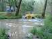 1978 Ford Bronco - A yellow Jeep CJ splashes through a muddy creek bed, with several people watching from the bank.