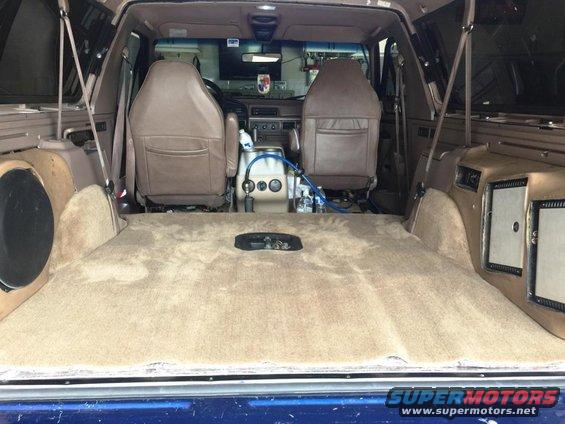 Interior of a 1996 Ford Bronco showing tan carpet, seats, and custom speaker boxes