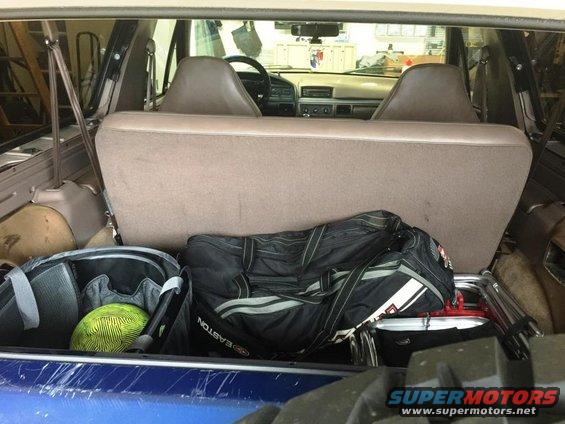 View of the back seats and cargo area of an older SUV, with sports bags and a yellow ball inside