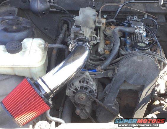 engine bay with shiny intake pipe and red air filter, alternator visible