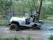 1978 Ford Bronco - A white Jeep CJ-7 navigates a muddy creek in a wooded area, with onlookers present.