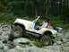 1978 Ford Bronco - A white Jeep CJ-7 tackles a challenging rocky trail with a driver behind the wheel.