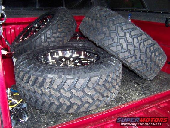 Red truck bed with three large off-road tires and chrome rims