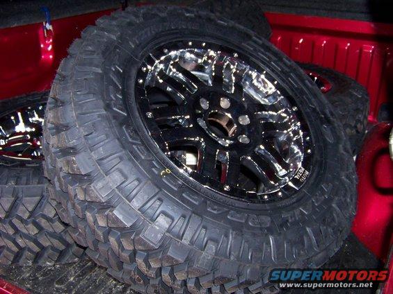 Aftermarket chrome wheels and mud tires stacked in a red truck bed
