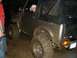 1978 Ford Bronco - A muddy off-road vehicle is driven by a person wearing a white cap.
