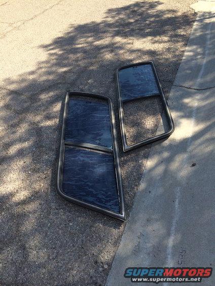 Two car door windows with dark tint and chrome trim lie on asphalt