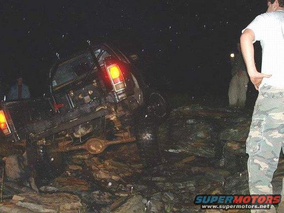 Off-road vehicle tilted on rocks at night, rear view showing taillights and suspension