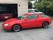1993 Mazda MX-3 - A red coupe with 'Quad Cam V6' badging is parked outside a garage with another car inside.