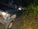 1978 Ford Bronco - A dark-colored SUV navigates a muddy trail at night, with dense foliage encroaching on the vehicle.