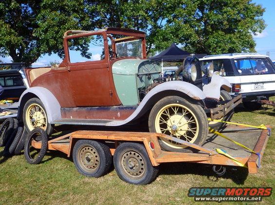 Brown and green antique convertible on an orange trailer, yellow spoked wheels, exposed engine
