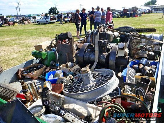 Trailer full of old engines, wheels, and assorted mechanical parts at an outdoor market