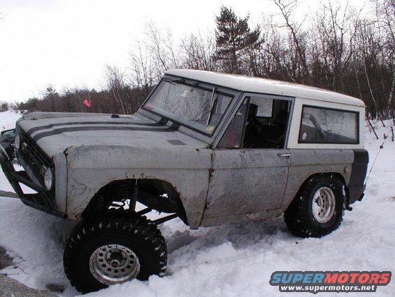Gray Ford Bronco with black racing stripes, lifted suspension, and large tires in the snow