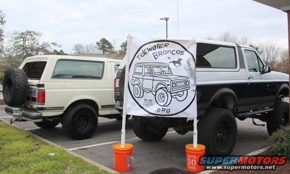 Two Ford Broncos parked, one white with spare tire on back, one black and white lifted. Banner reads 'Tidewater Broncos .Org'