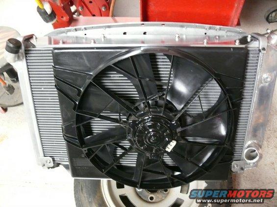 Radiator with black electric fan and silver aluminum end tanks, partially obscuring a silver wheel and tire