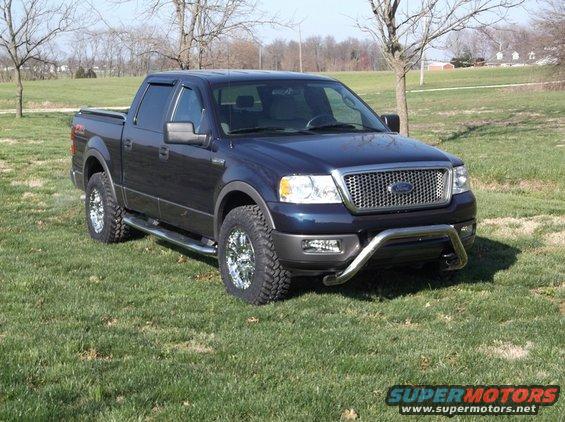 Dark blue Ford F-150 pickup truck with chrome grille and bull bar, parked on grass