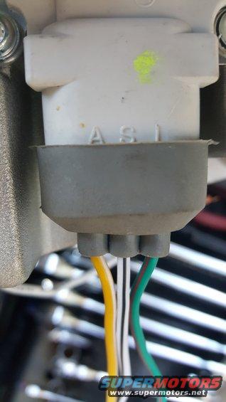 Close-up of a white electrical connector with a gray rubber boot, showing yellow, white, and green wires. Text 'ASI' is visible on the connector