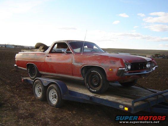 Red pickup truck on a trailer, front right side view. Has a spare tire in the bed