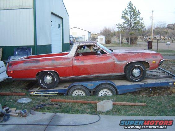 Red pickup truck on a trailer, parked outside a building