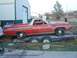 1971 Ford Ranchero - A red pickup truck with a white top is loaded onto a trailer, parked on grassy ground near a large building.