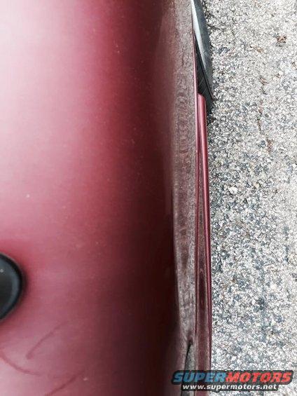 Maroon car door edge with visible panel gap and gravel on the ground