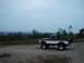 1994 Ford Bronco - A lifted, two-tone pickup truck sits on a dirt path with a city skyline visible in the distance under a cloudy sky.