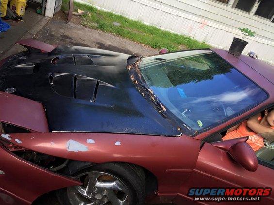 Customized sports car with a black hood with vents, maroon body, and a person in the passenger seat