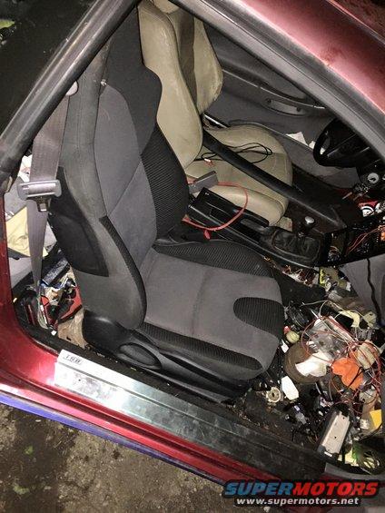 Interior view of a car with racing seats, roll cage, and messy wiring