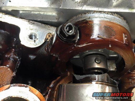 Close-up of engine components with oil residue and a bolt